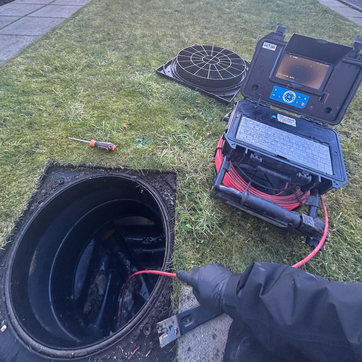 A CCTV drain survey in progress, with the camera in shot as well as the open drain cover.